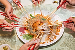 A group of people mixing and tossing Yee Sang dish with chop sticks. Yee Sang is a popular delicacy taken during Chinese New