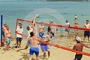A group of people playing volleyball on the beach. A clear, sunny summer day. People rest on vacation