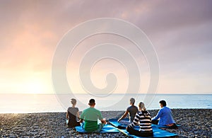 Group of people practicing morning meditation, yoga outdoors at sunrise on the beach. Feeling so comfortable and relax.