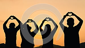 Group of people with raised arms and make hand to the heart shape looking at sunrise on the mountain background. Happiness,