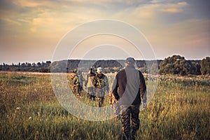 Group of people in a row going away through rural field at sunset during hunting season in countryside