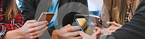 Group of people sitting around the table while holding smartphones - Teenagers obsessed with technology and using cellphones in