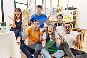 Group of people sitting at art studio celebrating victory with happy smile and winner expression with raised hands