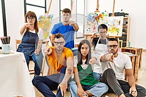 Group of people sitting at art studio pointing with finger to the camera and to you, confident gesture looking serious