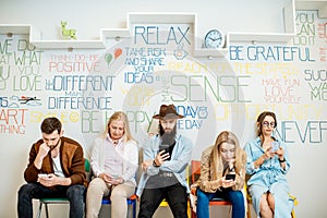 Group of people sitting in a row with smart phones indoors