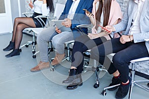 A group of people sitting in a waiting room near a white wall and using a mobile phone. Indoors.