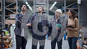 Group of people standing in warehouse looking up at stock racks talking. Positive confident female manager and male