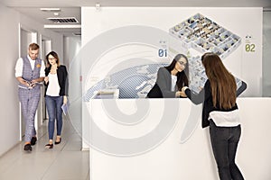 Group of people, two people walking, two women looking at papers in modern office hallway