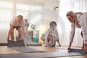 Group Of People Unrolling Exercise Mats Before Start Of Fitness Or Yoga Class In Community Center