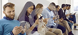 Group of young men and women sitting in office and text messaging on their mobile phones