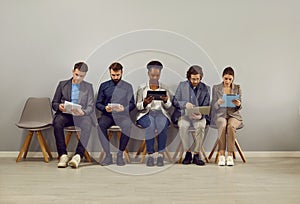 Group of people waiting for work meeting or job interview in line by gray office wall