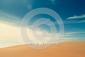 A group of people walks along the side of the desert. Blue sky.