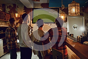 A group of people watching tv football in a sports bar.