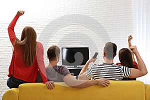 Group of people watching TV together on sofa in living room.