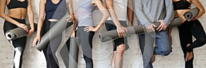 Group people wearing activewear holding yoga mats standing near wall