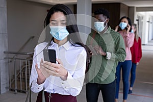 Group of people wearing face masks using smartphones while standing in queue