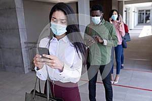 Group of people wearing face masks using smartphones while standing in queue