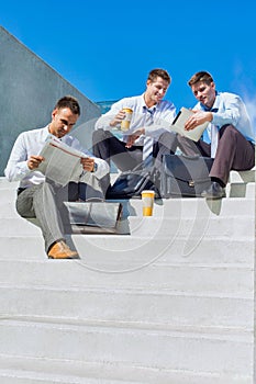 Group photo  of handsome businessman sitting on stairs while talking during break