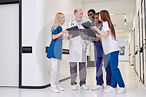 Group photo of young medics during conversation with senior confident doctor in hospital corridor