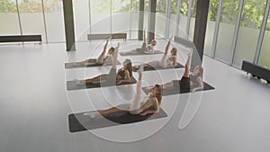 Group pilates classes. Six young women lying on floor and practicing leg swing exercise, training at light dance studio