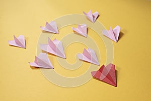 Group of pink paper aeroplane origami following the red one on yellow background