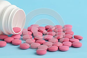 Group of pink round pills and white bottle on a blue background