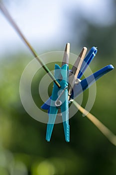 Group of plastic and light wooden clothes pegs hanging on clothesline in sunlight, green blurry background