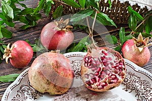 group of pomegranates on a rustic wooden table. A pomegranate cut into two parts inside a vintage plate