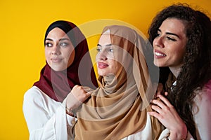 Group portrait of beautiful Muslim women two of them in a fashionable dress with hijab isolated on a yellow background