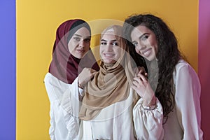 Group portrait of beautiful Muslim women two of them in a fashionable dress with hijab isolated on a yellow background