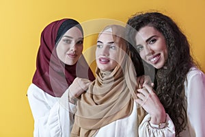 Group portrait of beautiful Muslim women two of them in a fashionable dress with hijab isolated on a yellow background