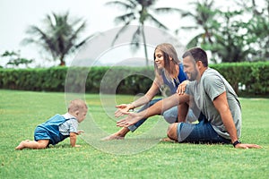 Group Portrait of cute young family. Baby crawling on green grass lawn during walk with her parents. Happy childhood and