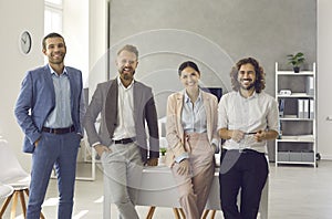 Team of happy young business people standing in modern office and smiling at camera
