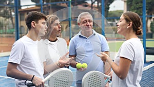 Group portrait of four padel players of different ages standing at tennis court at fitness health club