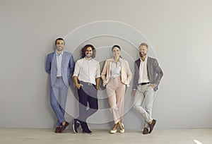 Group portrait of happy successful young business people standing by studio wall