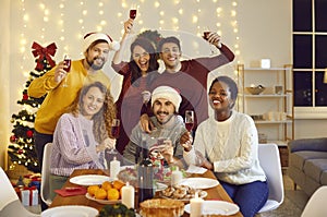 Group portrait of happy multiracial friends at dinner table at Christmas party at home