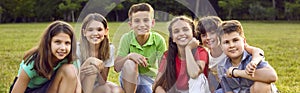 Group portrait of happy, smiling children sitting on green grass in the summer camp