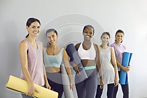 Group portrait of happy young women in activewear holding workout mats and smiling