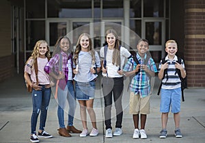 Group portrait of pre-adolescent school kids smiling in front of the school building