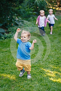 Group portrait of three white Caucasian blond adorable cute kids playing running in park garden outside