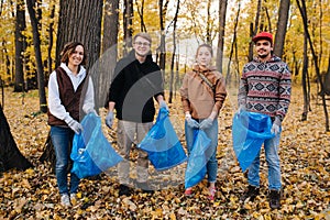 Group portrait of volunteers with trash bags in a seasonal forest at autumn