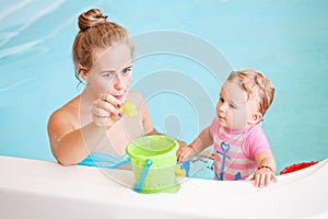 Group portrait of white Caucasian mother and baby daughter playing with toys in water on swimming poo nosing inside, training to