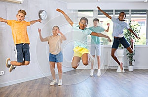Group of positive juvenile boys and girls jumping cheerfully in dancehall