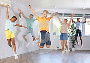 Group of positive juvenile boys and girls jumping cheerfully in dancehall