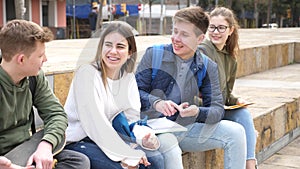 Group of positive teenagers having fun together sitting on steps outdoors at big city