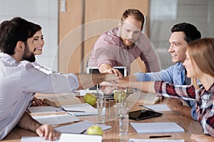 Group of positive workers holding hands together over workplace