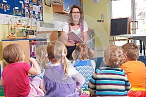 Group Of Pre School Children Listening To Teacher Reading Story