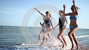 Group of pretty female friends running by the sea on sandy tropical beach in swimsuits. Interracial women in bikini have