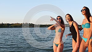 Group of pretty female friends walking by the sea on sandy tropical beach in swimsuits. Interracial women in bikini