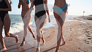 Group of pretty girls friends running by the sea on sandy tropical beach in swimsuits. Interracial women in bikini have